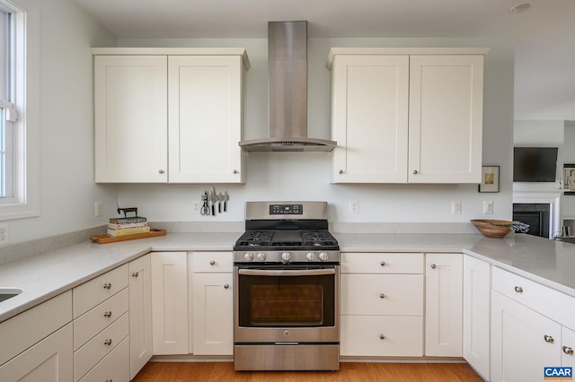 kitchen featuring white cabinetry, stainless steel range with gas cooktop, light hardwood / wood-style floors, and wall chimney exhaust hood