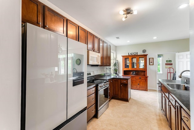 kitchen with dark countertops, a sink, stainless steel appliances, recessed lighting, and a peninsula