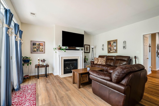 living area with visible vents, a fireplace with flush hearth, light wood-style flooring, and baseboards
