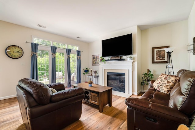 living area with baseboards, visible vents, a glass covered fireplace, and light wood-type flooring