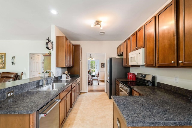 kitchen featuring stainless steel appliances, dark countertops, a sink, and a peninsula