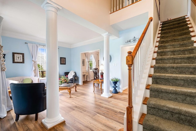 foyer entrance featuring stairs, ornate columns, crown molding, and light wood finished floors