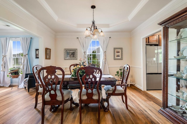 dining room with plenty of natural light, a raised ceiling, light wood-style flooring, and a notable chandelier