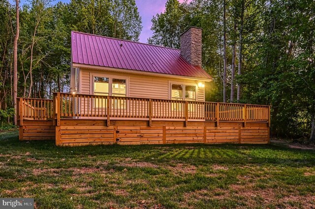 back house at dusk with a deck and a lawn