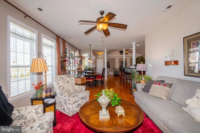 living room with a ceiling fan, decorative columns, wood finished floors, and visible vents