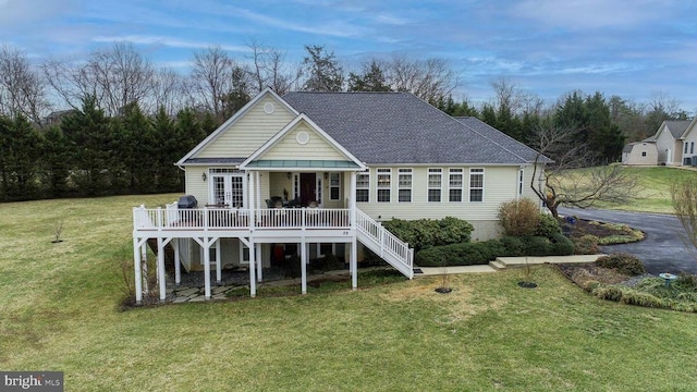 rear view of property featuring a deck, stairway, a lawn, and a shingled roof