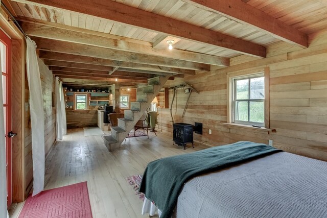 unfurnished bedroom featuring beamed ceiling, a wood stove, wooden ceiling, and wood walls