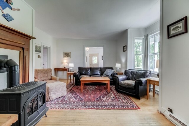 living room featuring a wood stove, baseboard heating, and light hardwood / wood-style flooring