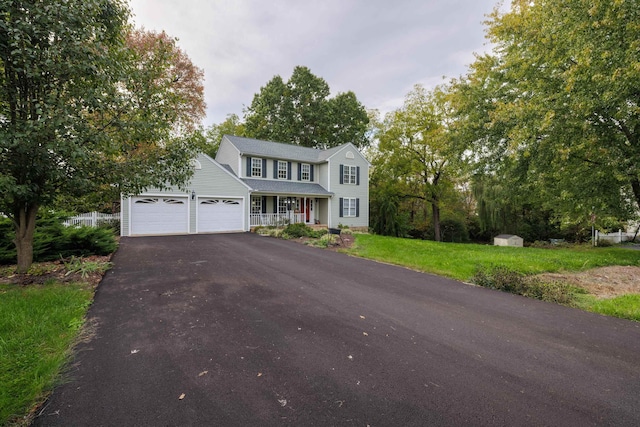 colonial home with fence, aphalt driveway, a front yard, covered porch, and a garage