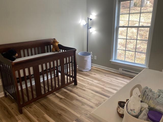 bedroom featuring light wood finished floors, baseboard heating, and baseboards