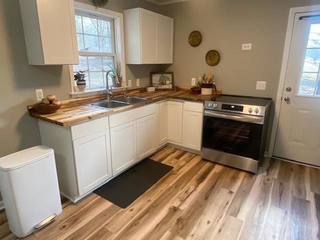 kitchen featuring stainless steel range with electric stovetop, white cabinets, a healthy amount of sunlight, and a sink