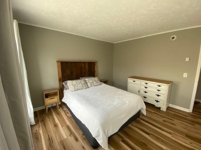 bedroom with a textured ceiling, wood finished floors, and baseboards