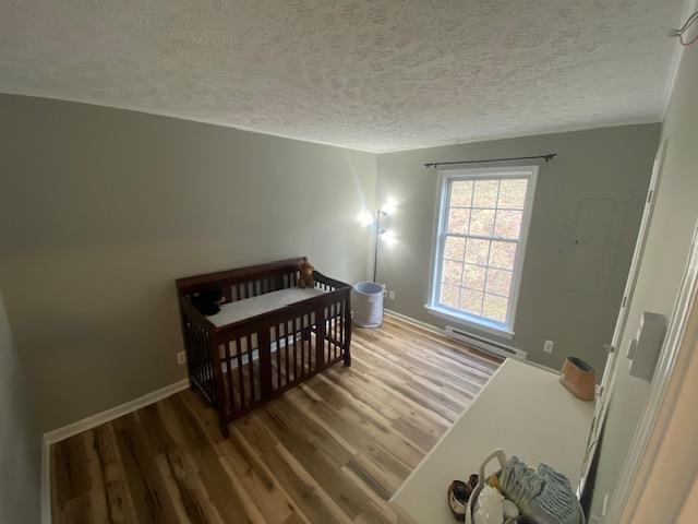 bedroom featuring a baseboard radiator, a textured ceiling, wood finished floors, a nursery area, and baseboards