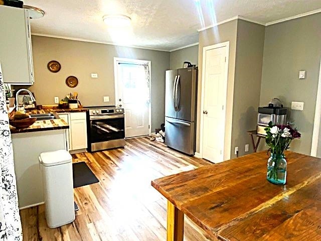 kitchen featuring stainless steel appliances, light wood-style flooring, ornamental molding, a sink, and a textured ceiling