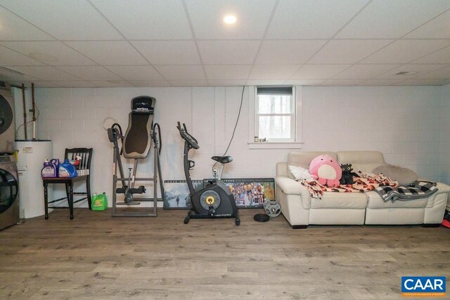 basement featuring concrete block wall, a drop ceiling, wood finished floors, and electric water heater