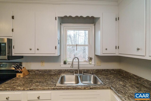 kitchen featuring stainless steel microwave, a sink, white cabinetry, and crown molding