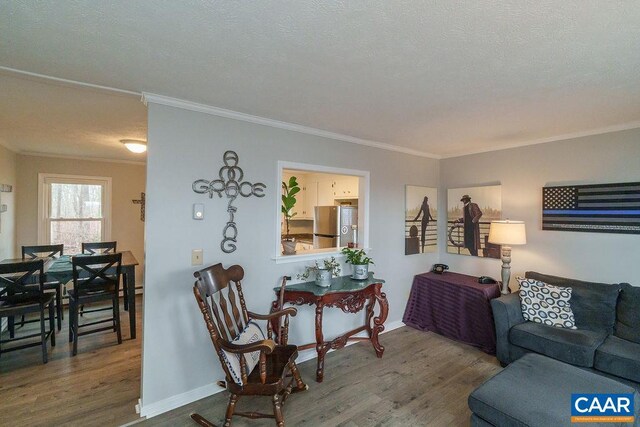 living area featuring baseboards, a textured ceiling, ornamental molding, and wood finished floors