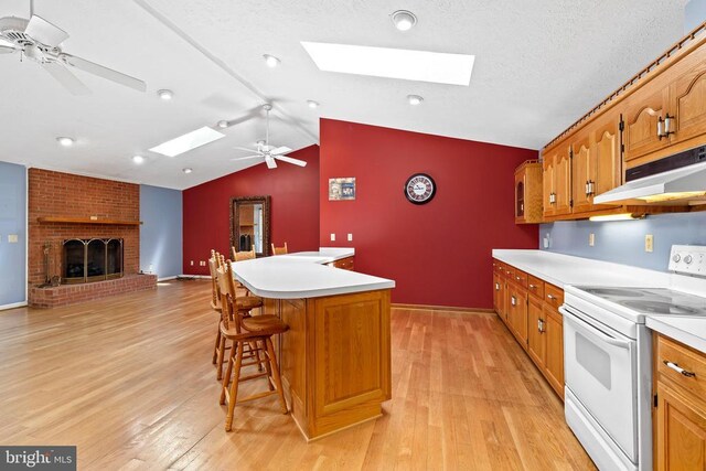 kitchen with white electric range oven, a breakfast bar, a kitchen island, ceiling fan, and a fireplace