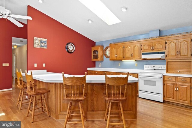 kitchen featuring a breakfast bar area, lofted ceiling with skylight, light hardwood / wood-style floors, a kitchen island, and white electric stove