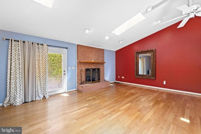 unfurnished living room featuring ceiling fan, a fireplace, light hardwood / wood-style floors, and lofted ceiling with skylight