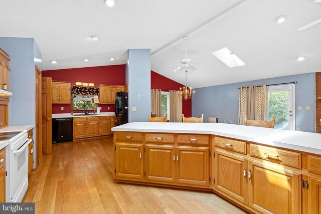 kitchen with ceiling fan with notable chandelier, vaulted ceiling with skylight, sink, black appliances, and light wood-type flooring