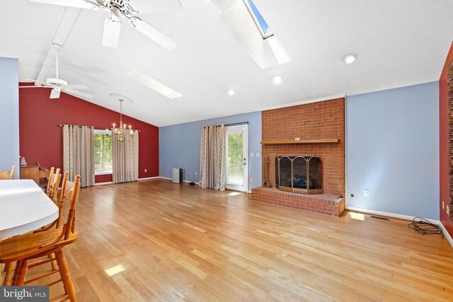 living room with vaulted ceiling with skylight, a fireplace, ceiling fan with notable chandelier, and light wood-type flooring