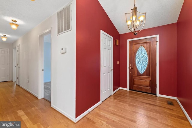 entryway with an inviting chandelier, hardwood / wood-style floors, lofted ceiling, and a textured ceiling