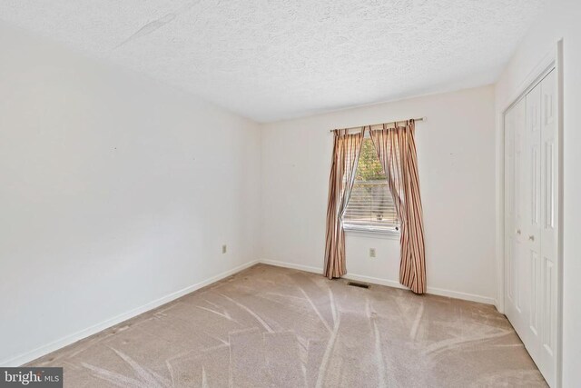 spare room featuring light colored carpet and a textured ceiling