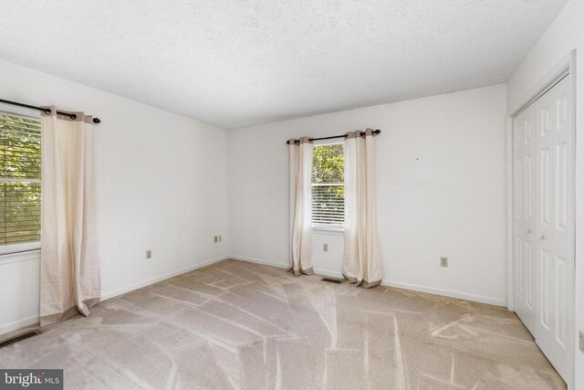 unfurnished bedroom featuring light carpet, a textured ceiling, and a closet