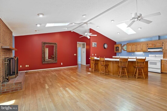 kitchen featuring white electric range, light hardwood / wood-style flooring, ceiling fan, a kitchen breakfast bar, and a brick fireplace