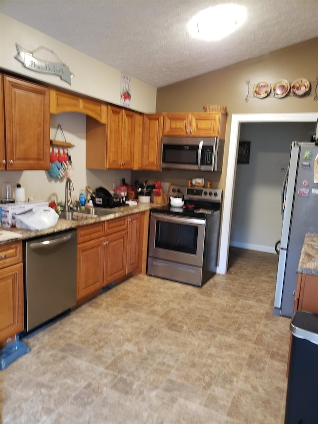 kitchen featuring sink, vaulted ceiling, stainless steel appliances, and a textured ceiling