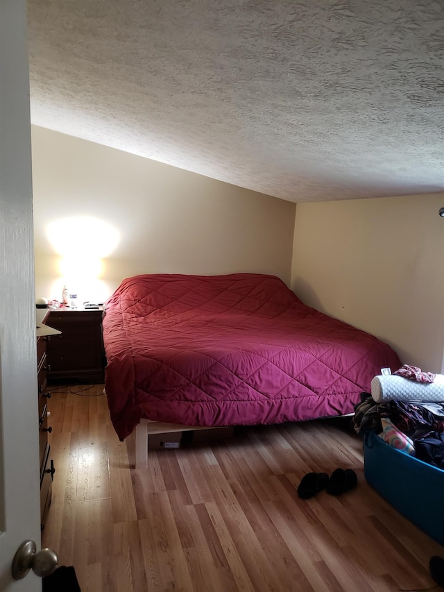 bedroom featuring hardwood / wood-style flooring, vaulted ceiling, and a textured ceiling