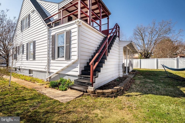 view of property exterior featuring stairway, fence, and a lawn