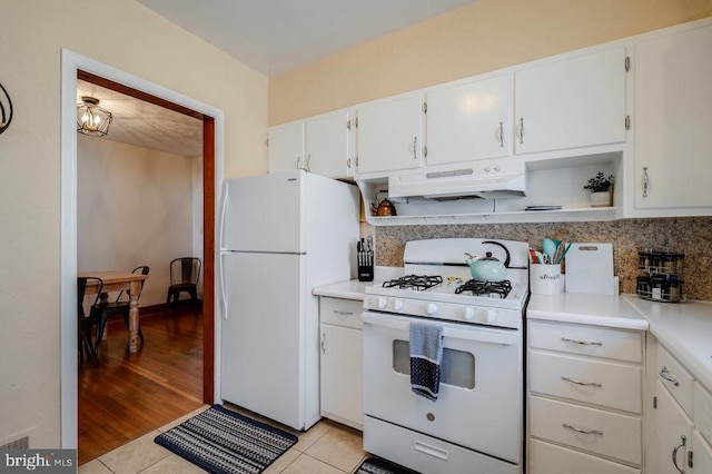 kitchen featuring under cabinet range hood, white appliances, white cabinetry, and light countertops