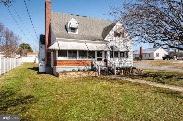 new england style home featuring a front lawn, fence, a shingled roof, brick siding, and a chimney