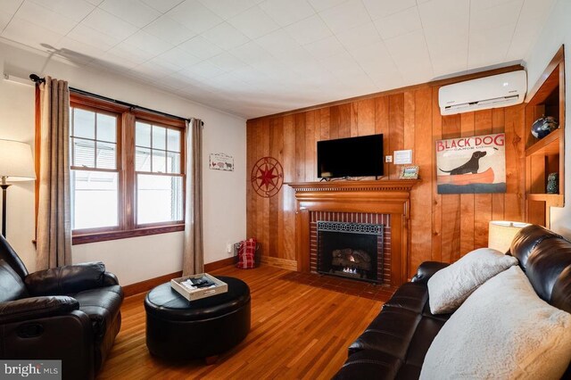 living room featuring wooden walls, wood finished floors, a fireplace, and a wall mounted AC