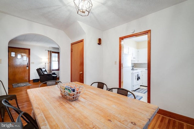 dining space featuring arched walkways, a textured ceiling, baseboards, and wood finished floors