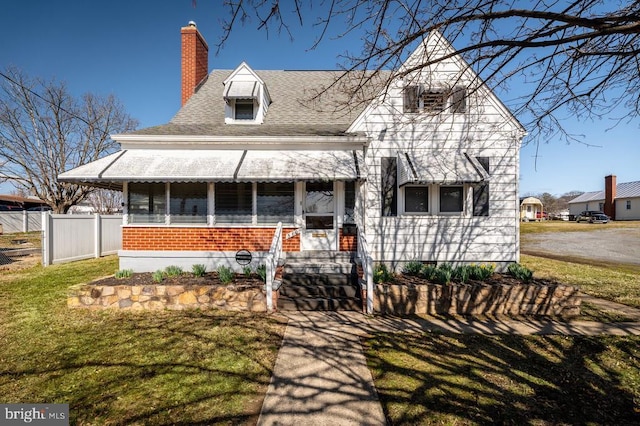 view of front of home featuring brick siding, a chimney, a front lawn, and fence