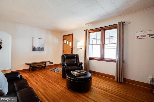 living area featuring visible vents, arched walkways, baseboards, and light wood finished floors