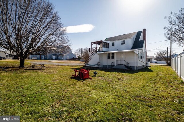 back of house with a balcony, a yard, fence, and a chimney