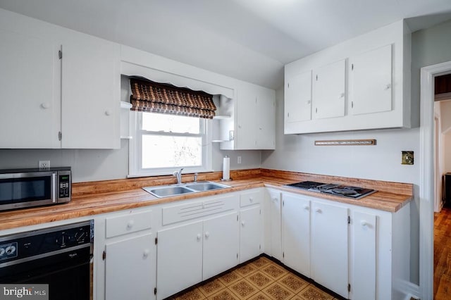 kitchen with a sink, stainless steel microwave, light countertops, and white cabinetry