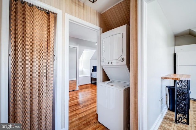 laundry area featuring wood finished floors, baseboards, wallpapered walls, laundry area, and stacked washer / dryer