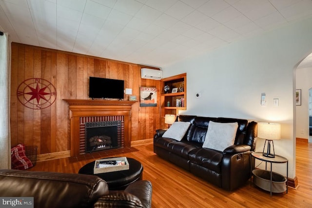 living room with built in shelves, wood finished floors, arched walkways, and a wall mounted air conditioner