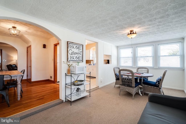 carpeted dining space with arched walkways, a textured ceiling, and baseboards