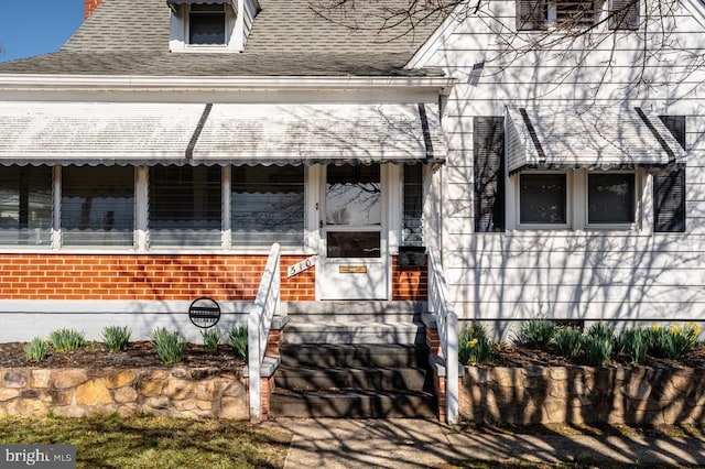 property entrance featuring brick siding and roof with shingles