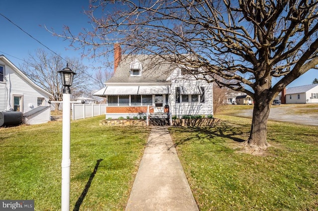 view of front facade with brick siding, a front lawn, fence, a chimney, and heating fuel