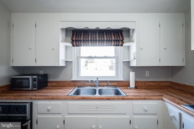 kitchen with stainless steel microwave, open shelves, white cabinets, wood counters, and a sink