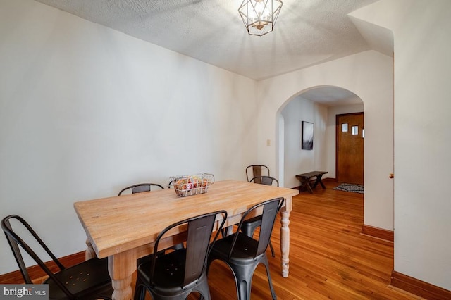 dining space featuring baseboards, wood finished floors, arched walkways, and a textured ceiling