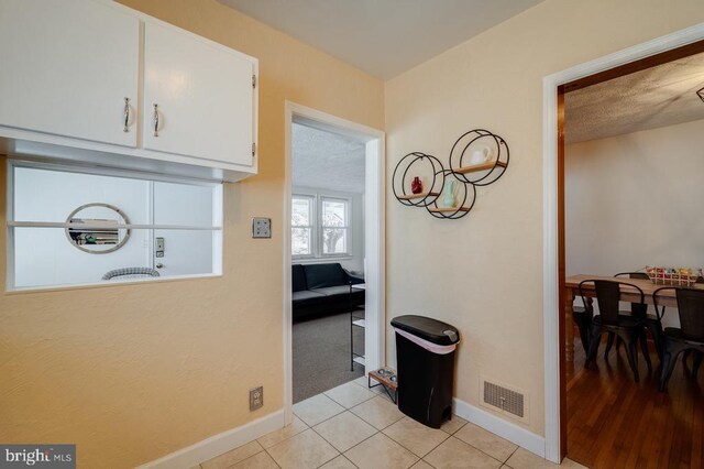 corridor featuring light tile patterned floors, visible vents, and baseboards