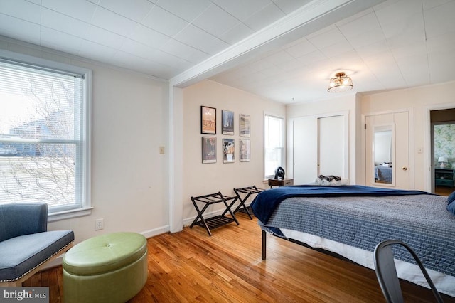 bedroom featuring multiple windows, crown molding, light wood-type flooring, and baseboards